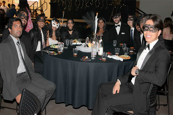 2025 Masquerade Gala men and women sitting at a table, wearing masks and dressed in semi-formal attire