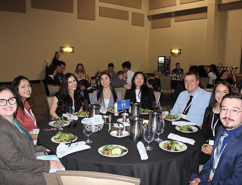 men and women sitting at a round table with plates of salad in front of them