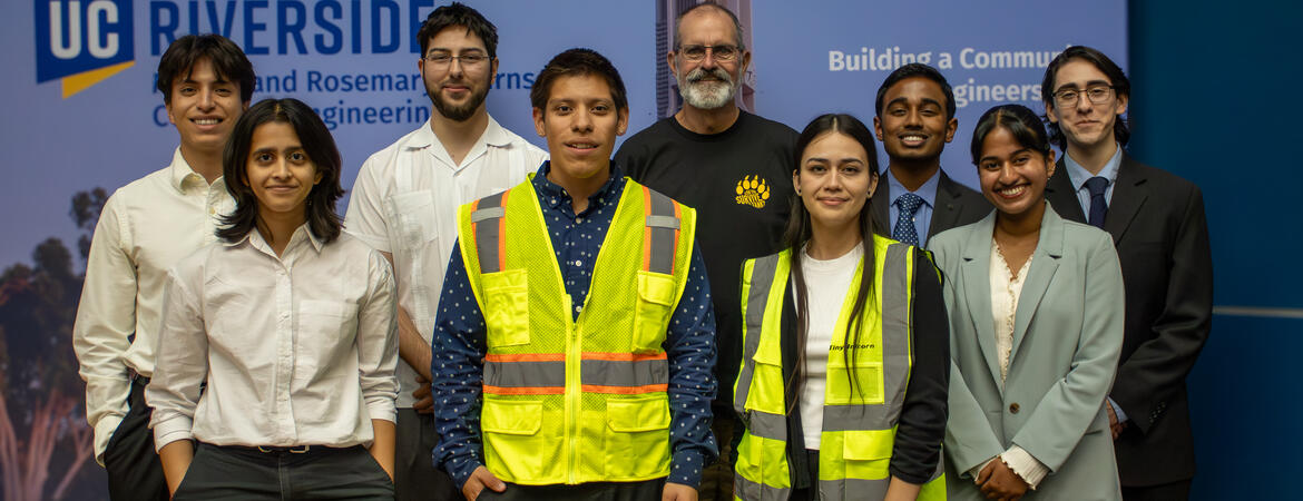 A group of UCR engineering students and a faculty member pose together following a student project presentation, with two students wearing high-visibility safety vests.