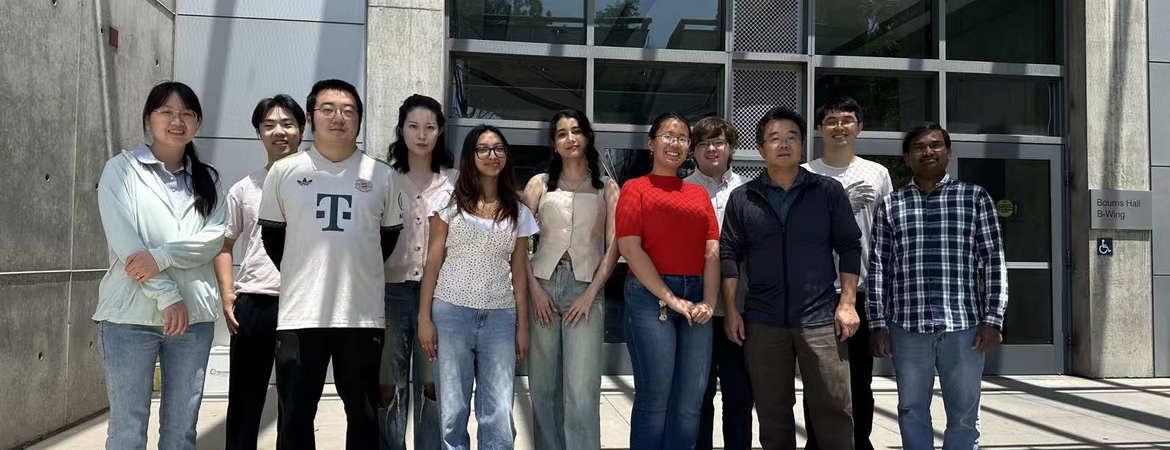 A group of eleven students and faculty members standing outside the Bourns College of Engineering building entrance on a sunny day, posing together for a group photo.