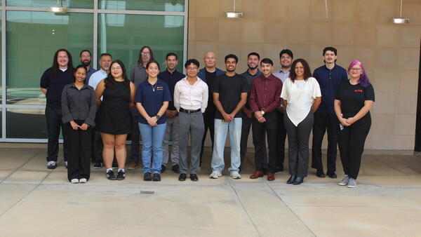 BCOE summer research students and mentors gather for a group photo outside a glass-fronted campus building.