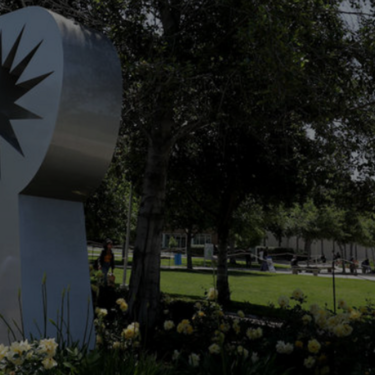 UCR campus sign surrounded by landscaping and trees near a campus walkway.
