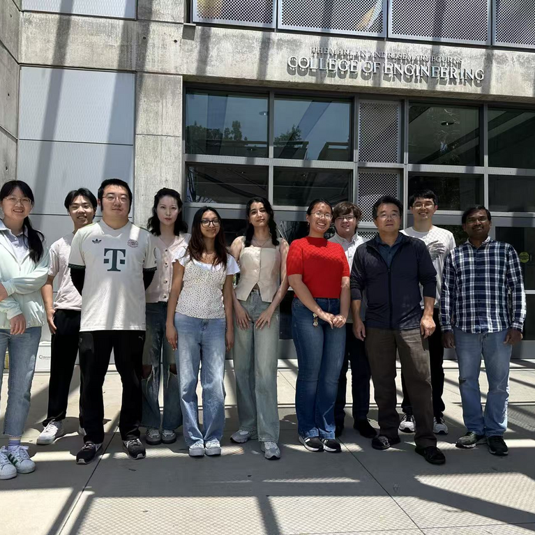 A group of eleven students and faculty members standing outside the Bourns College of Engineering building entrance on a sunny day, posing together for a group photo.