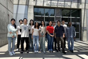 A group of eleven students and faculty members standing outside the Bourns College of Engineering building entrance on a sunny day, posing together for a group photo.