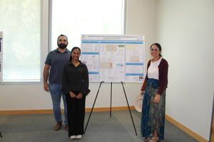 Three participants pose beside a research poster at the BCOE Summer Research Symposium.
