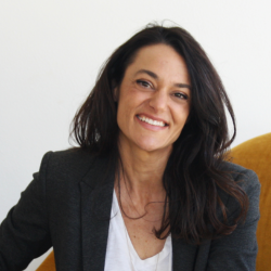 Annika Speer, a woman with dark hair, wearing a dark blazer over a white shirt, smiling at the camera.