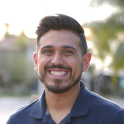 Sam Tapia a smiling man with dark hair and a beard, wearing a dark blue collared shirt.