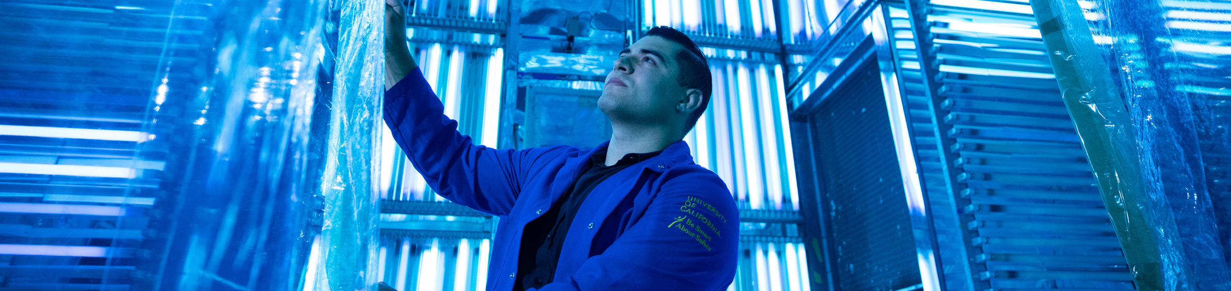 Engineering student inspects materials inside a blue-lit environmental testing chamber.