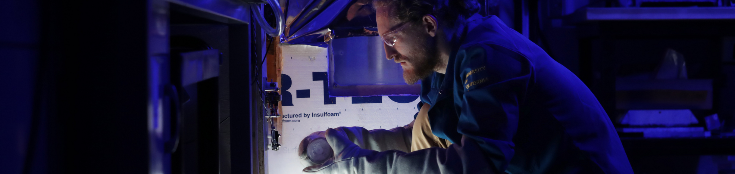 Graduate researcher conducts materials testing inside a temperature-controlled lab enclosure.