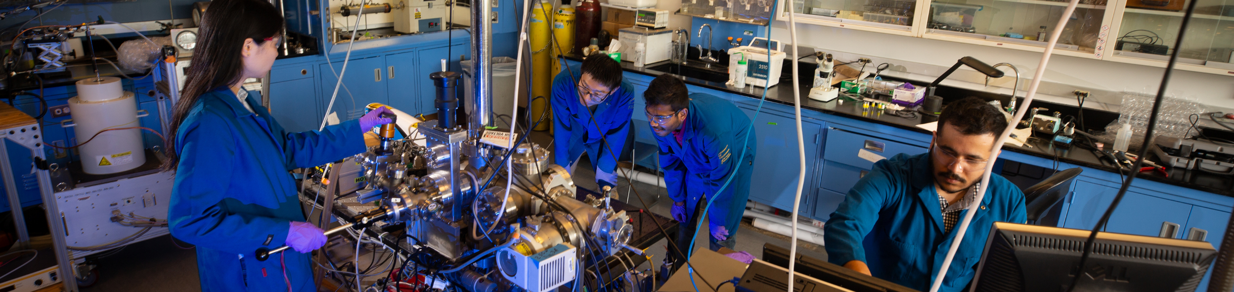 Four engineering students collaborate around advanced lab equipment, monitoring an experiment.