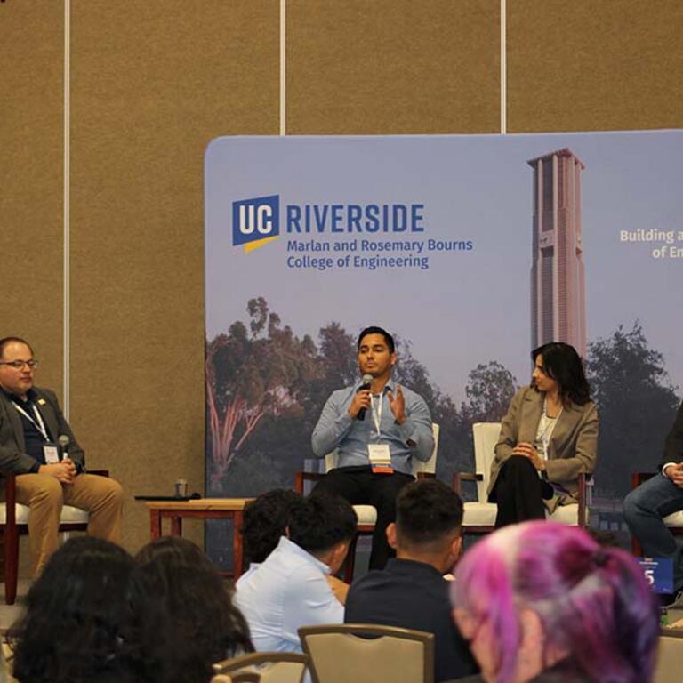 three men and one woman sitting on a stage holding microphones