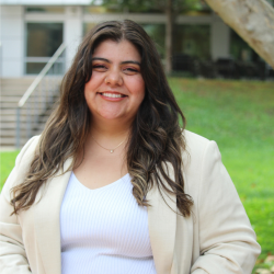 Fernanda Rojas wearing a tan blazer and jeans standing outdoors smiling  