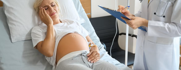 a young pregnant woman with blond hair laying on a hospital bed with a medical professional standing by the bed