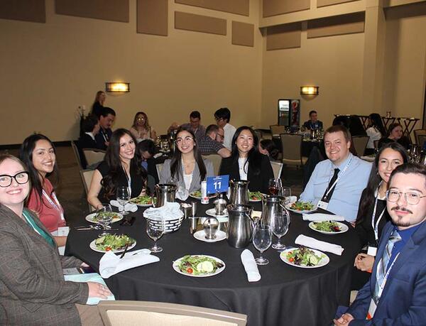 men and women sitting at a round table with plates of salad in front of them