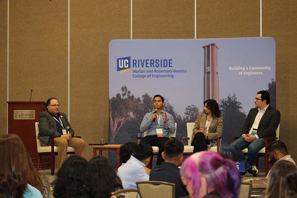 three men and one woman sitting on a stage holding microphones