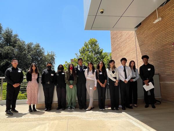 A dozen students dressed in professional attire stand posed on the Winston Chung Hall patio