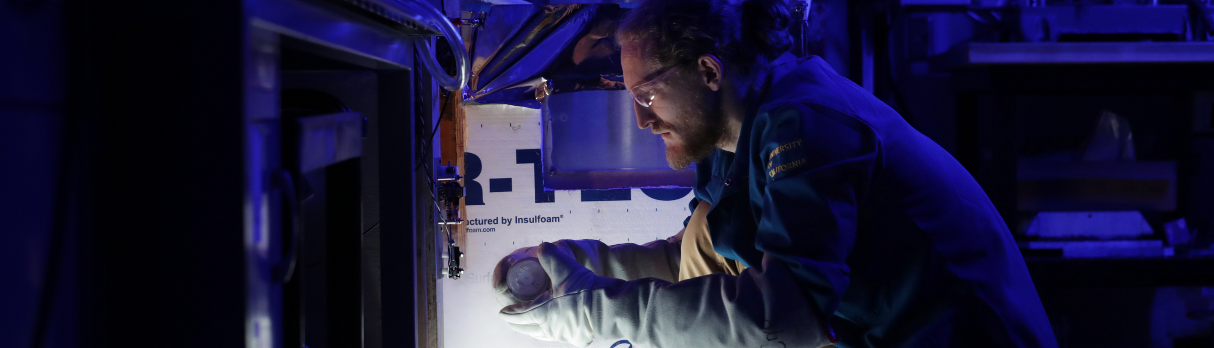 Graduate researcher conducts materials testing inside a temperature-controlled lab enclosure.