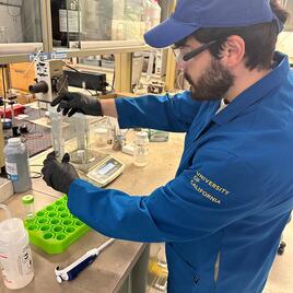 Javier in the lab bearded male student wearing working in a lab wearing gloves, a blue ball cap, blue lab coat