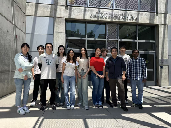A group of eleven students and faculty members standing outside the Bourns College of Engineering building entrance on a sunny day, posing together for a group photo.